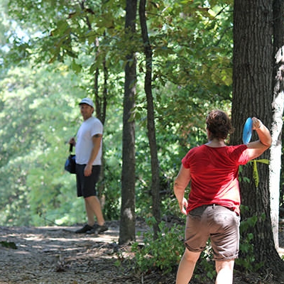 A golfer throws her disc in a heavily shaded part of the course